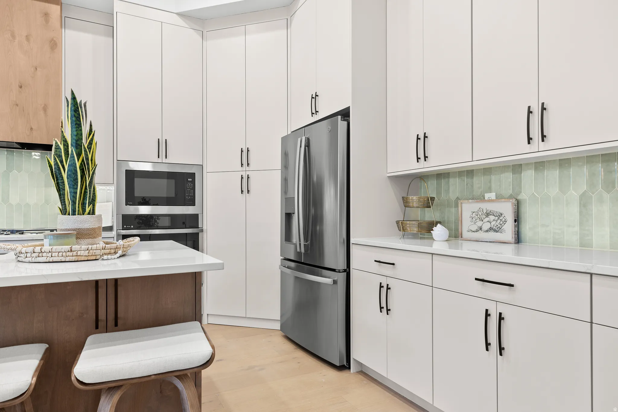 Modern kitchen featuring light cabinetry with dark hardware, stainless steel appliances, a built-in microwave, and a green picket tile backsplash
