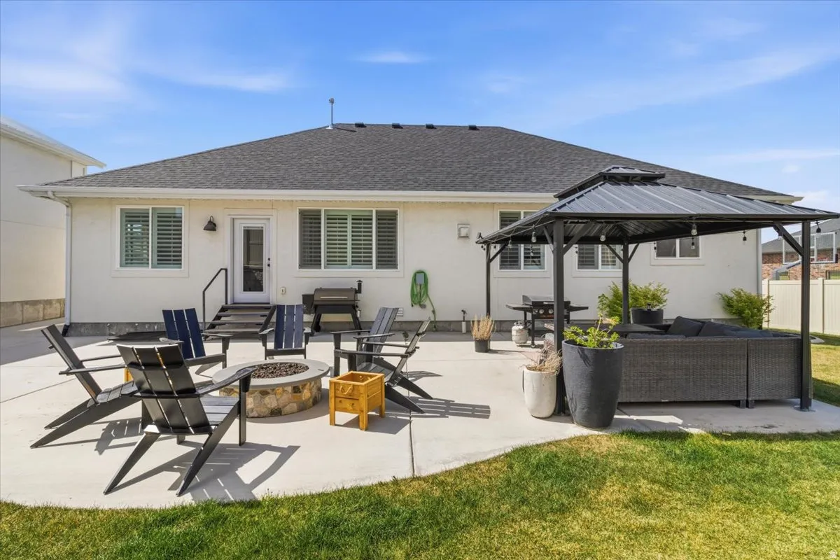 Rear view of property featuring an outdoor living space with a fire pit, a shingled roof, a patio, stucco siding, and a gazebo