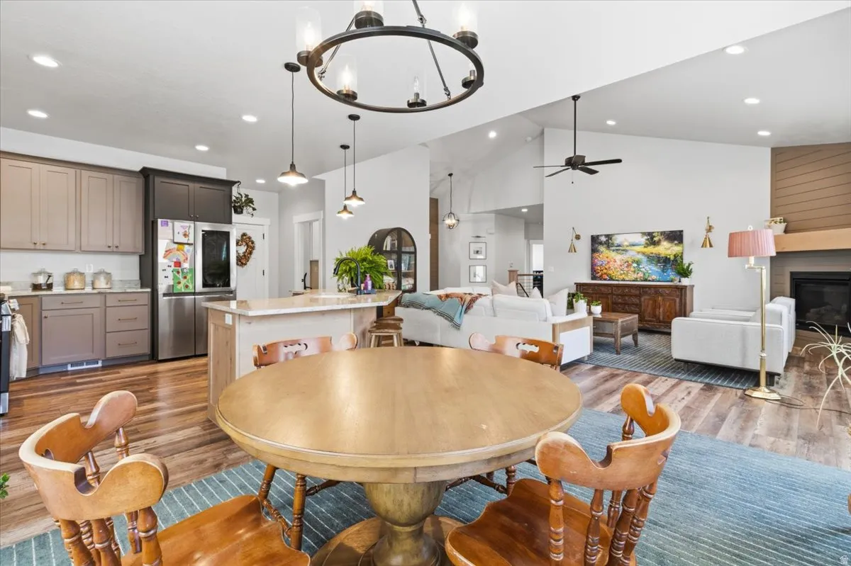 Dining room with light wood-style flooring, hanging lights, a fireplace, vaulted ceiling, and ceiling fan
