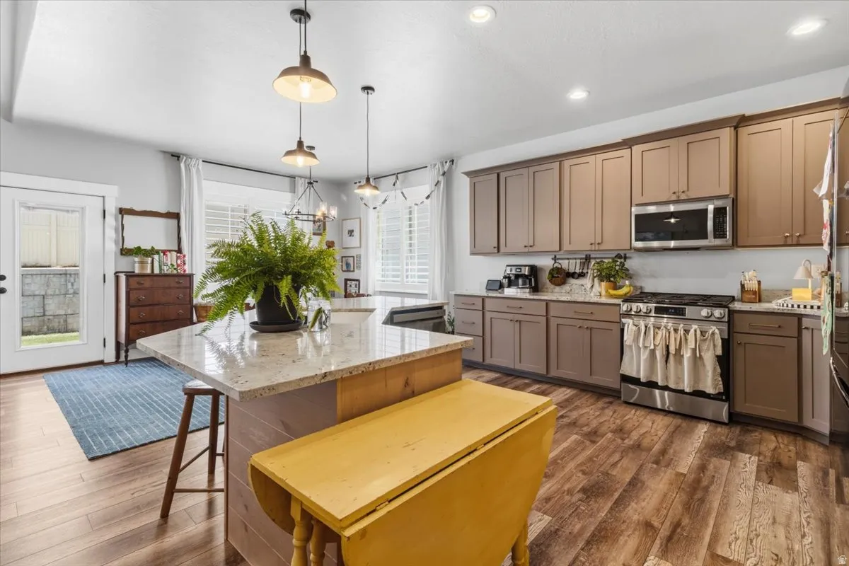 Kitchen with stainless steel appliances, light stone counters, dark wood-style flooring, a kitchen breakfast bar, and a kitchen island