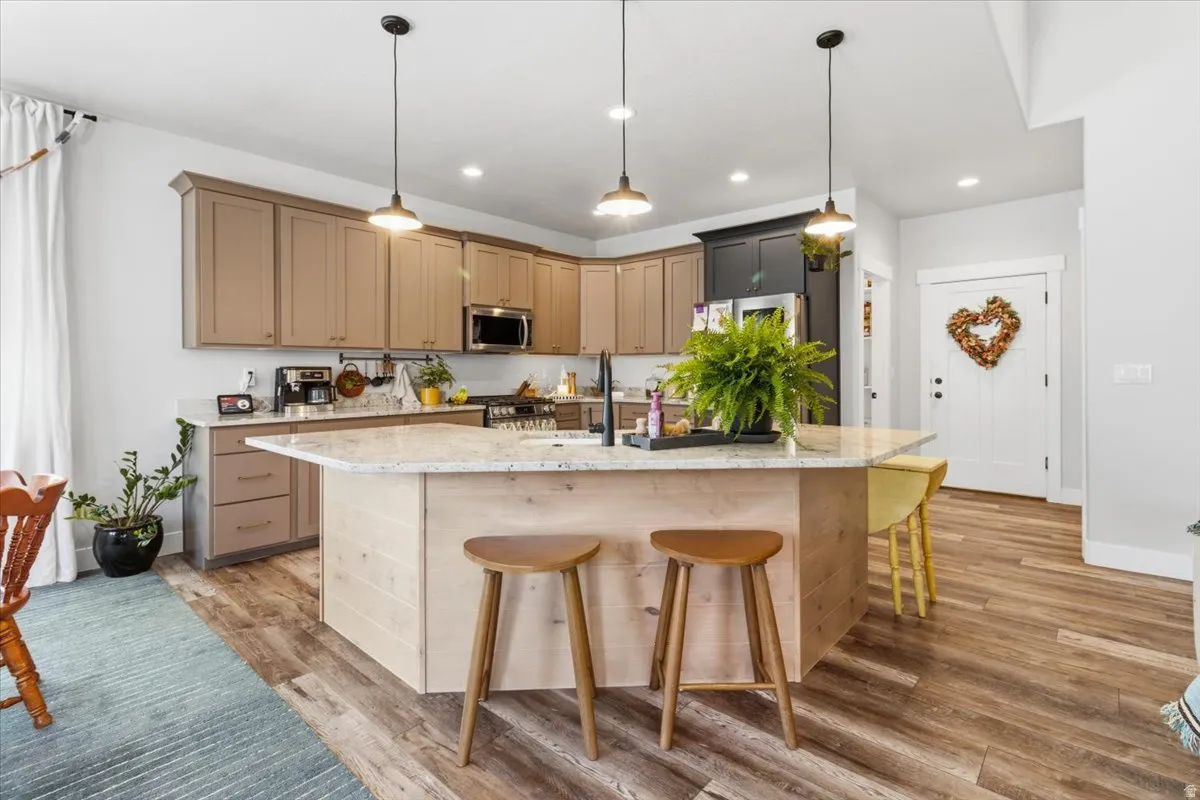 Kitchen featuring light stone counters, light wood finished floors, a breakfast bar area, a center island with sink, and hanging light fixtures