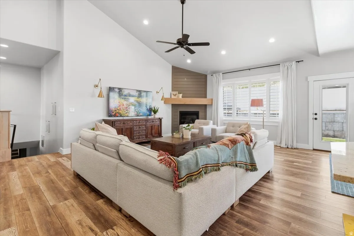 Living room with lofted ceiling, light wood-style flooring, a glass covered fireplace, ceiling fan, and recessed lighting