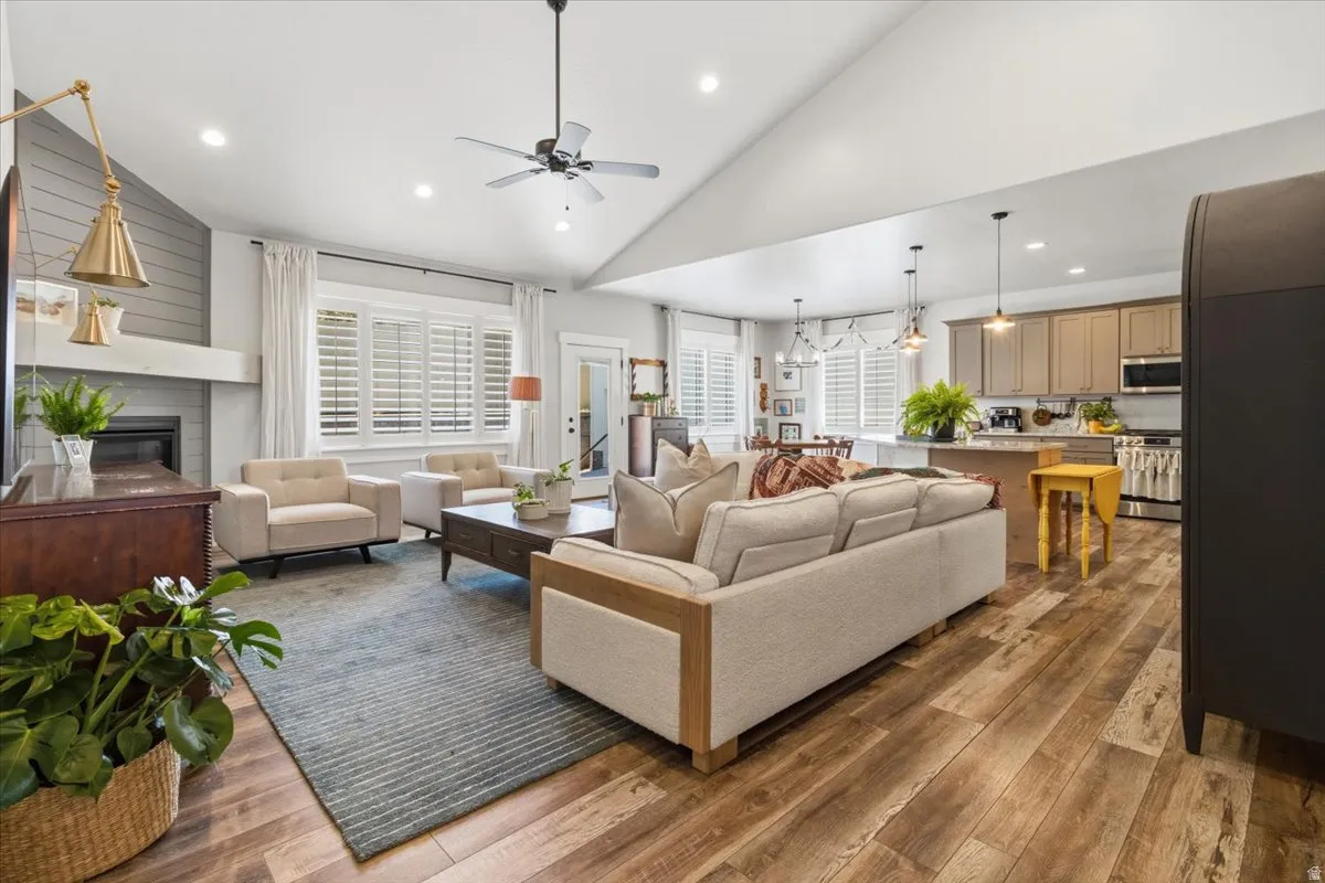 Living area featuring vaulted ceiling, wood-type flooring, recessed lighting, a ceiling fan, and a glass covered fireplace