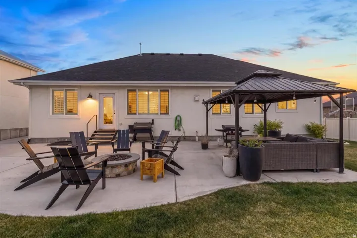 Back of property at dusk with an outdoor living space with a fire pit, a patio, and roof with shingles