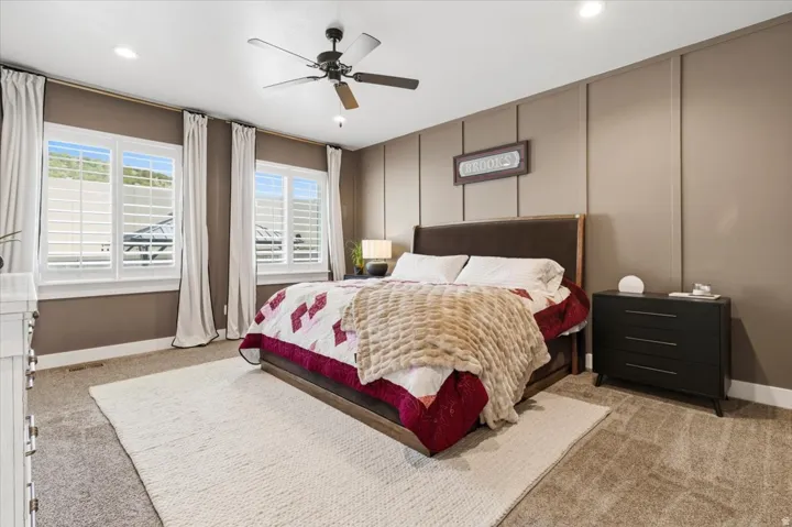 Bedroom with light colored carpet, a ceiling fan, a decorative wall, and recessed lighting