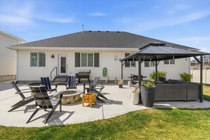Rear view of property featuring an outdoor living space with a fire pit, a shingled roof, a patio, stucco siding, and a gazebo