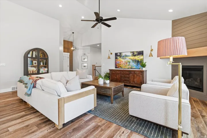 Living area featuring a glass covered fireplace, light wood finished floors, lofted ceiling, ceiling fan, and recessed lighting