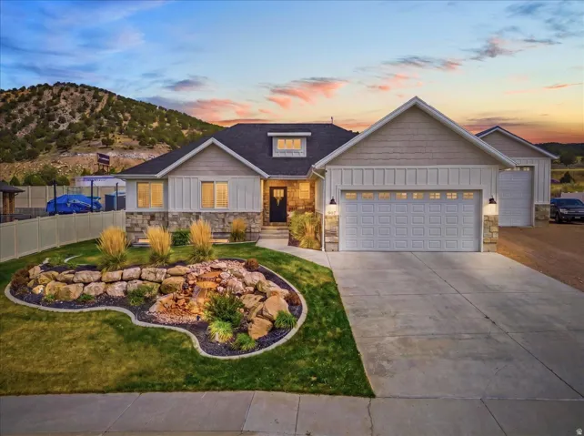 View of front of home with board and batten siding, stone siding, a garage, and driveway