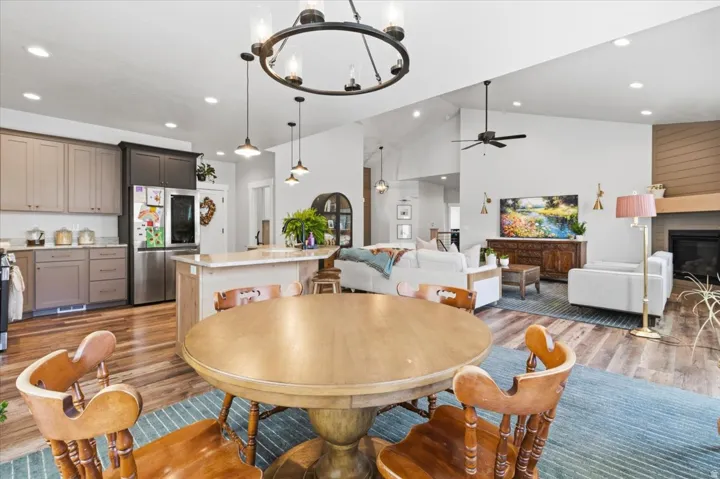 Dining room with light wood-style flooring, hanging lights, a fireplace, vaulted ceiling, and ceiling fan