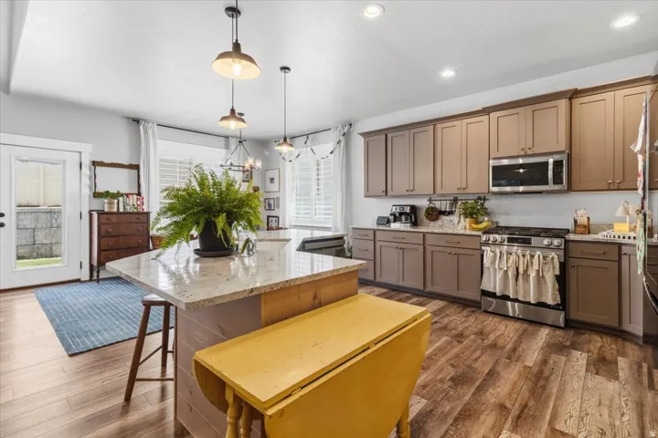 Kitchen with stainless steel appliances, light stone counters, dark wood-style flooring, a kitchen breakfast bar, and a kitchen island