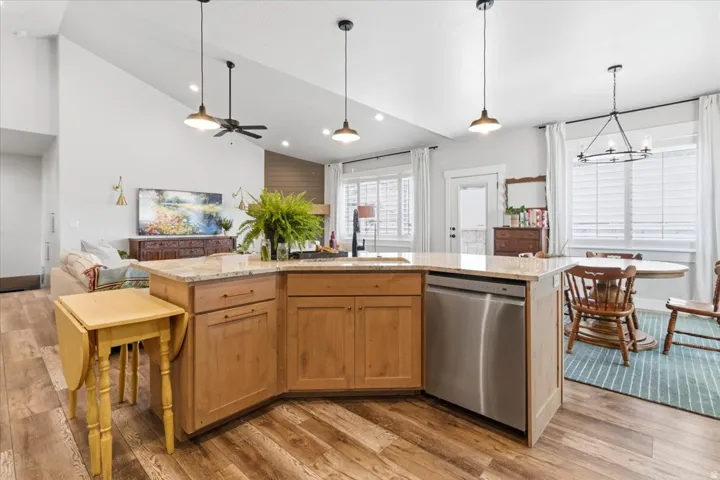 Kitchen featuring an island with sink, light stone counters, open floor plan, light wood-type flooring, and lofted ceiling