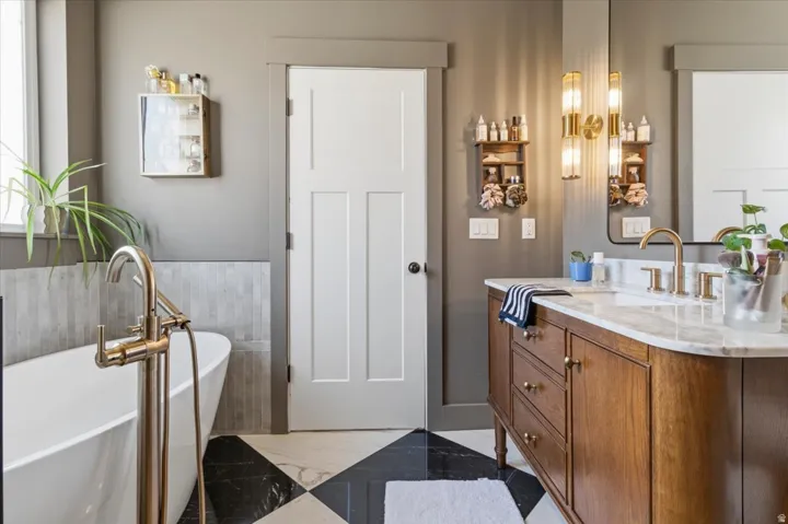 Bathroom with vanity, a freestanding tub, light marble finish floors, and a wainscoted wall