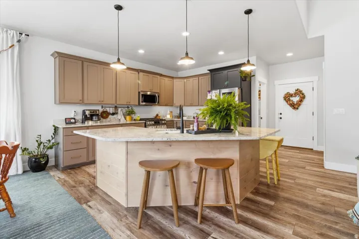 Kitchen featuring light stone counters, light wood finished floors, a breakfast bar area, a center island with sink, and hanging light fixtures