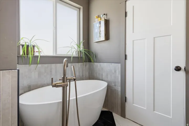 Full bathroom with a soaking tub, a wainscoted wall, and tile walls