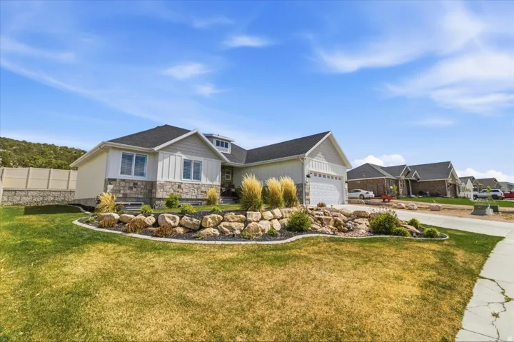 View of front of home featuring stone siding, board and batten siding, an attached garage, a front lawn, and driveway