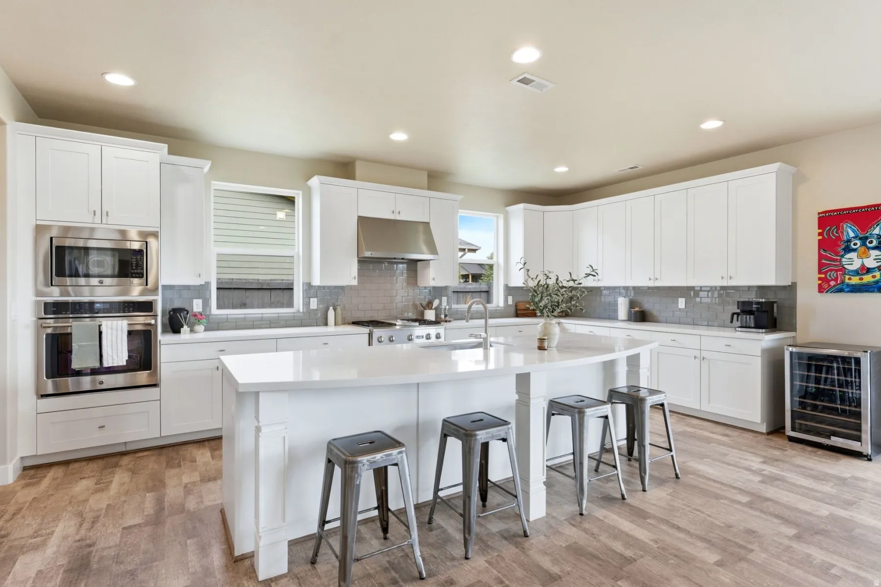 Kitchen featuring stainless steel appliances, beverage cooler, a breakfast bar, white cabinetry, and a kitchen island with sink