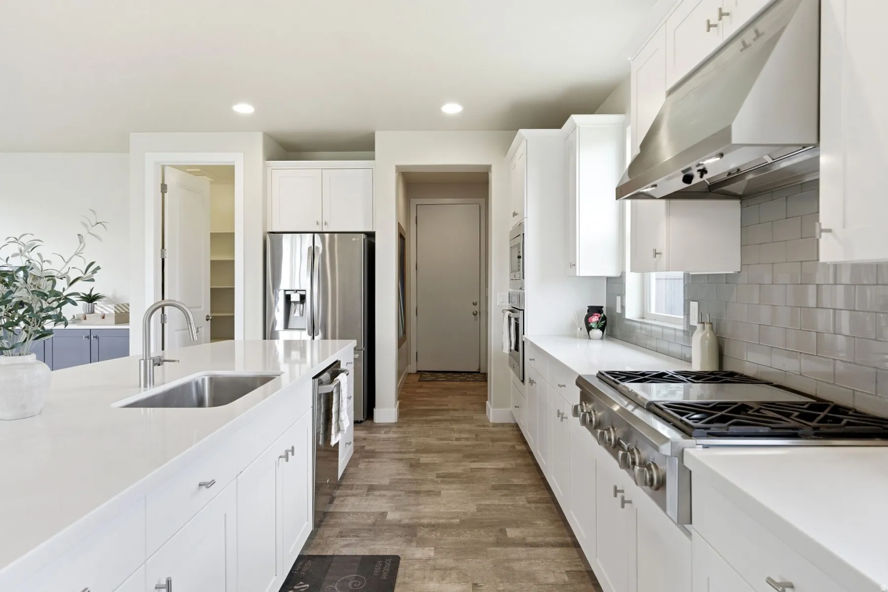 Kitchen with stainless steel appliances, white cabinets, light wood finished floors, tasteful backsplash, and recessed lighting