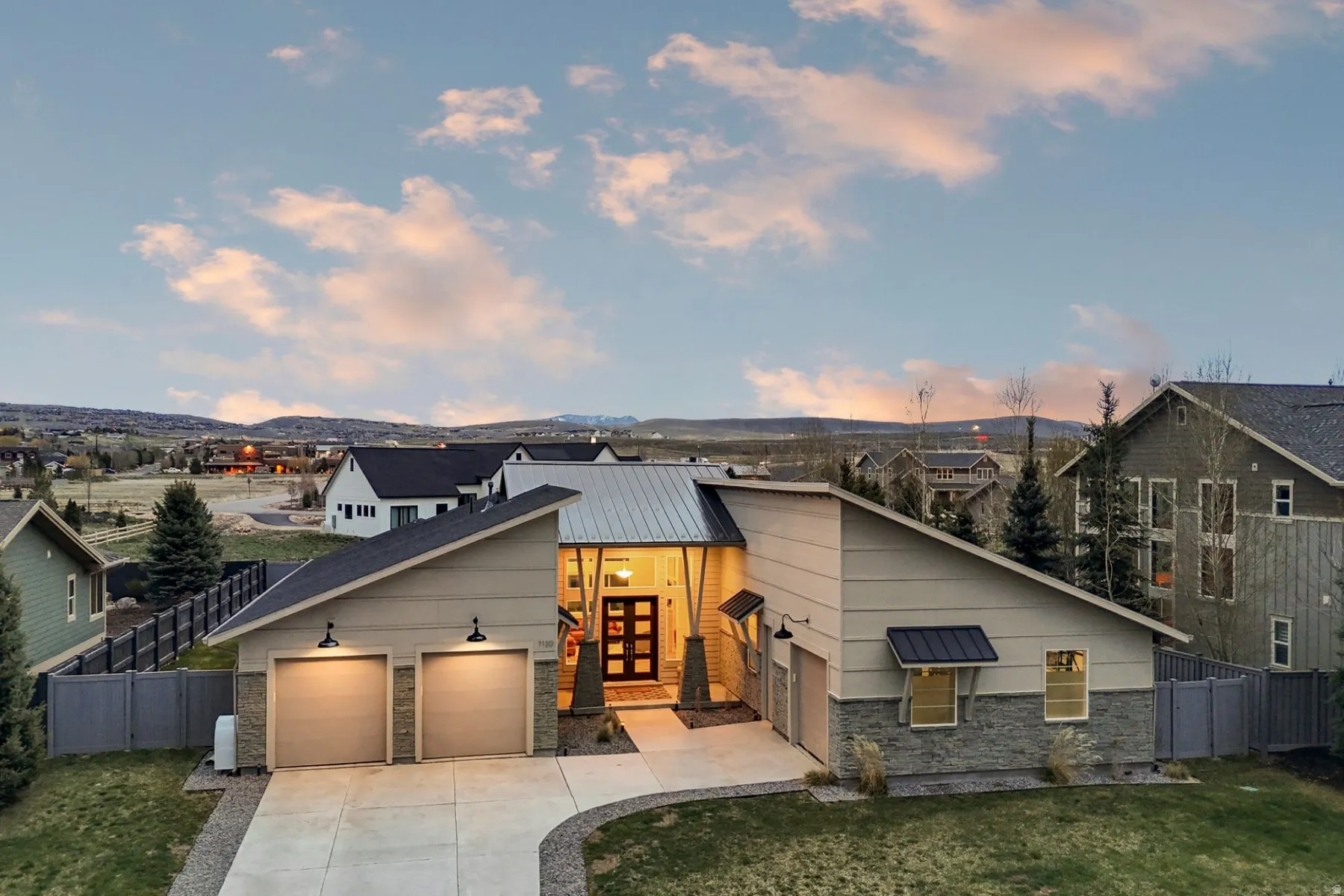 Contemporary house featuring stone siding, driveway, an attached garage, and a metal roof