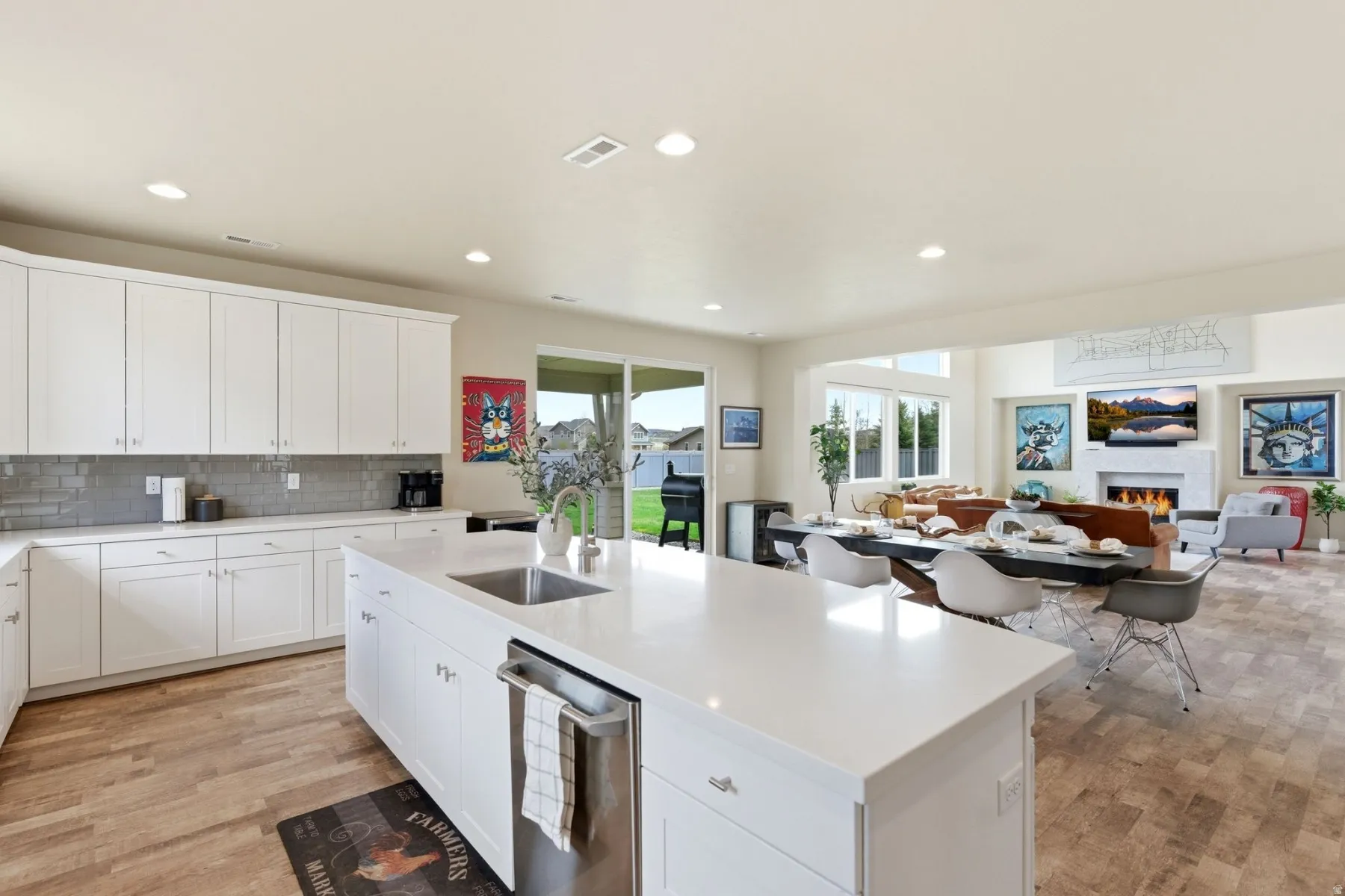 Kitchen featuring light wood-type flooring, open floor plan, a lit fireplace, white cabinets, and a kitchen island with sink