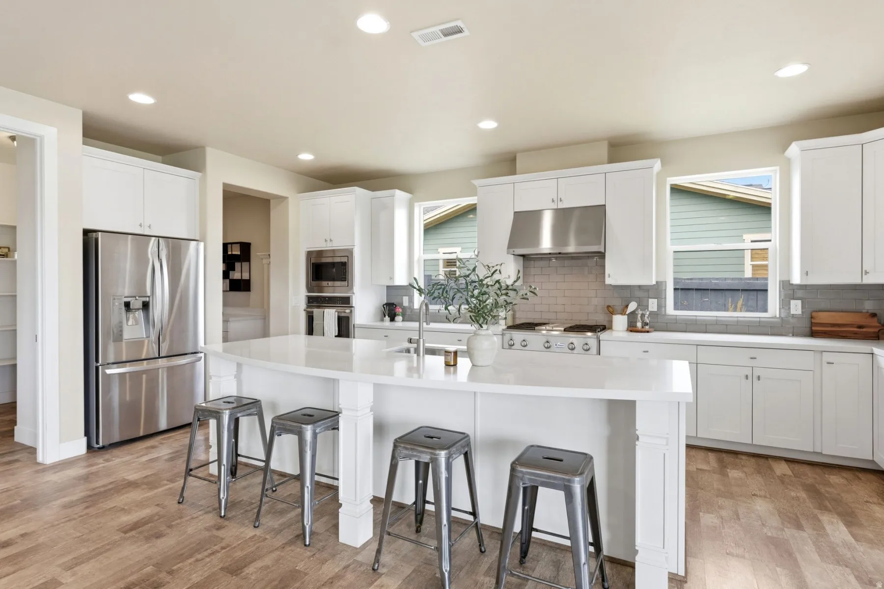 Kitchen with stainless steel appliances, a breakfast bar area, a kitchen island with sink, light wood-style flooring, and white cabinetry