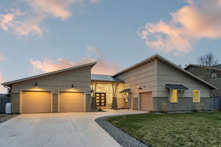 Contemporary home featuring an attached garage, concrete driveway, a front yard, french doors, and a metal roof