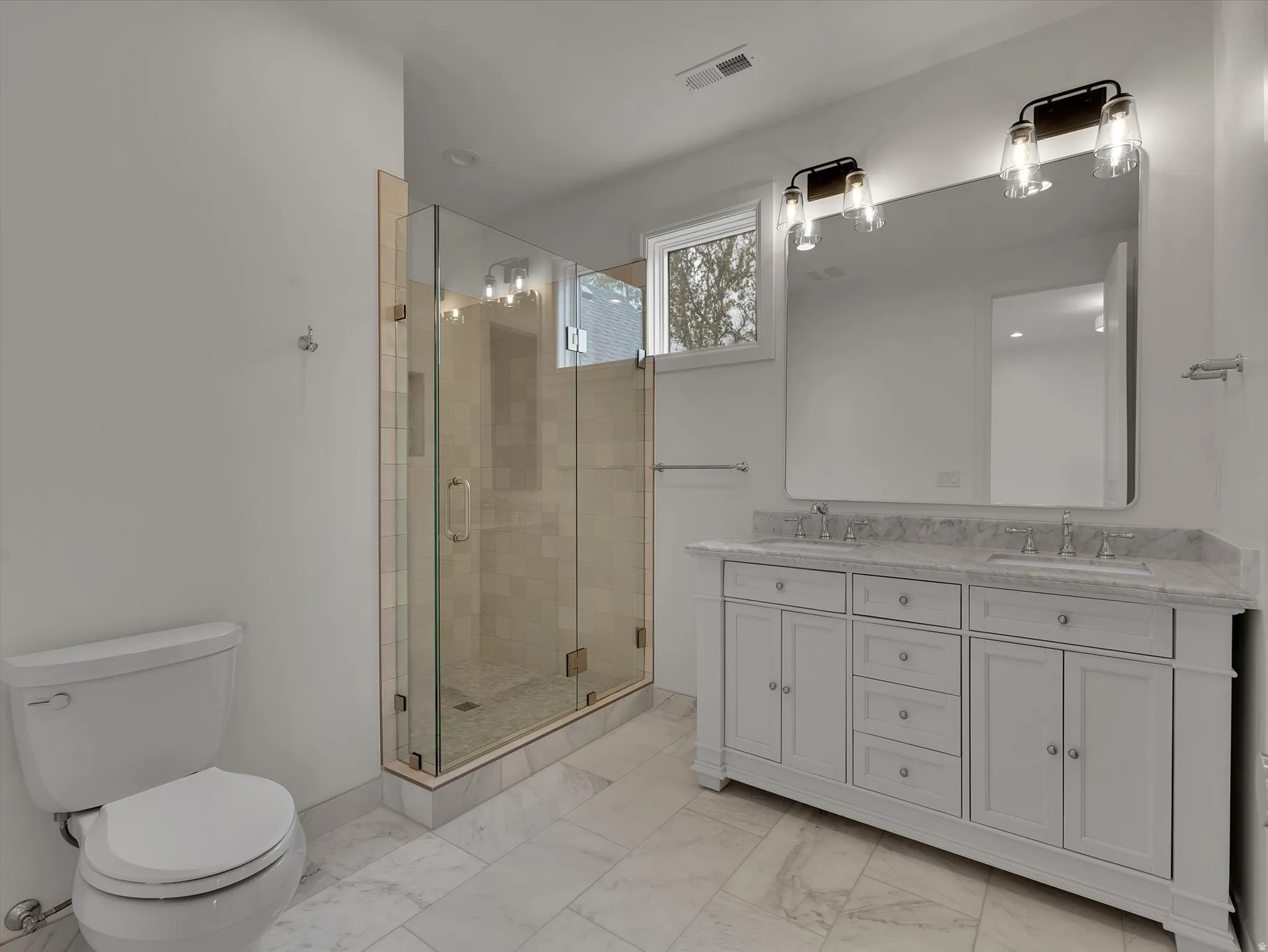 Full bathroom featuring double vanity, a stall shower, and light marble finish floors