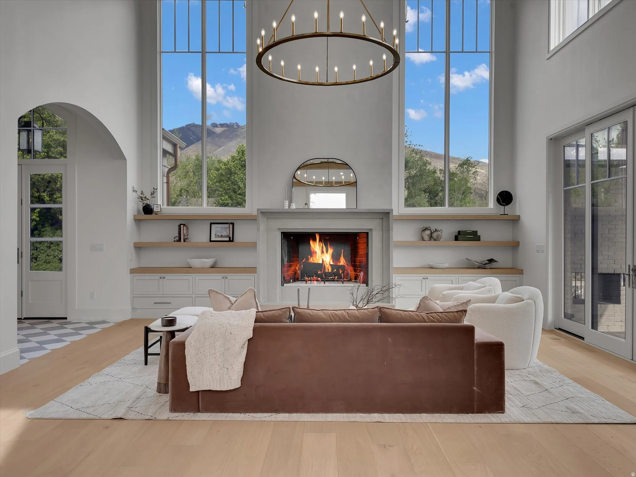 Living room featuring a high ceiling, a lit fireplace, light wood-type flooring, a mountain view, and arched walkways