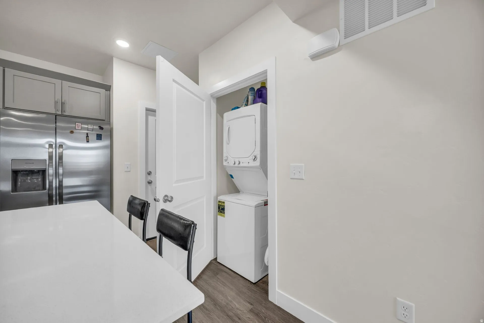 Kitchen featuring stainless steel refrigerator with ice dispenser, stacked washer and dryer, a kitchen bar, dark wood-type flooring, and gray cabinetry