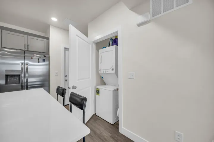 Kitchen featuring stainless steel refrigerator with ice dispenser, stacked washer and dryer, a kitchen bar, dark wood-type flooring, and gray cabinetry