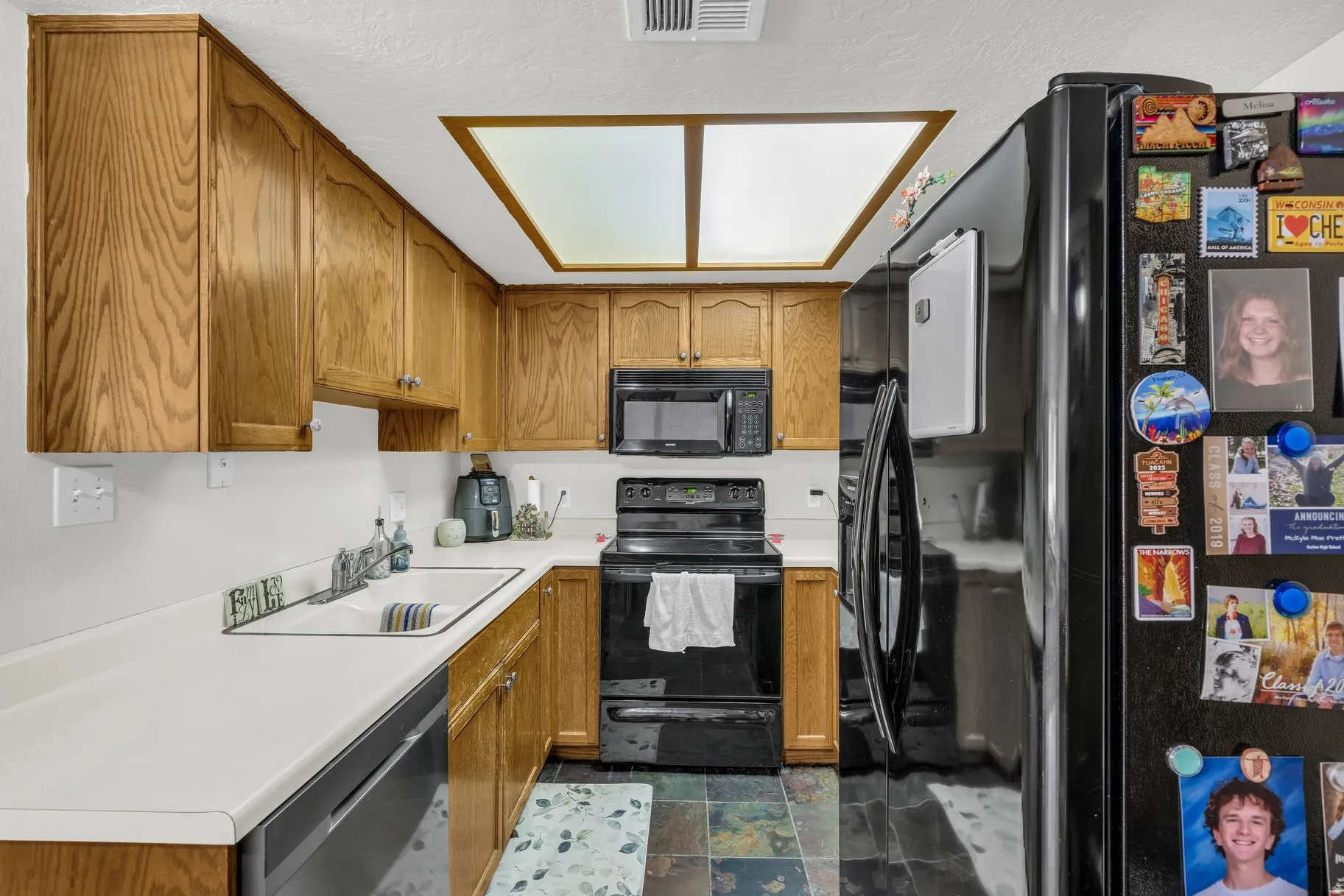 Kitchen featuring black appliances, wood finish cabinetry, light countertops, and stone finish flooring
