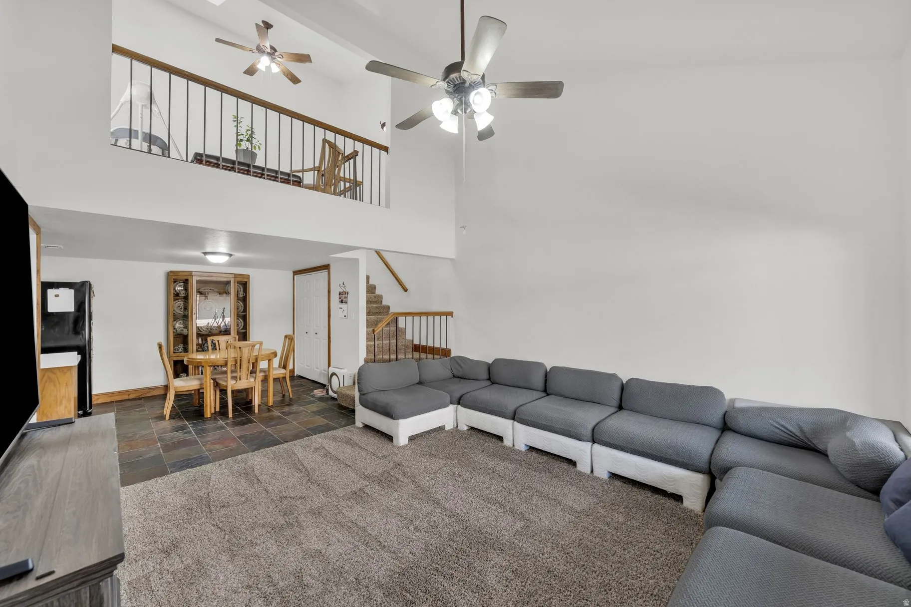 Living room featuring stone tile floors, a ceiling fan, dark carpet, and a high ceiling