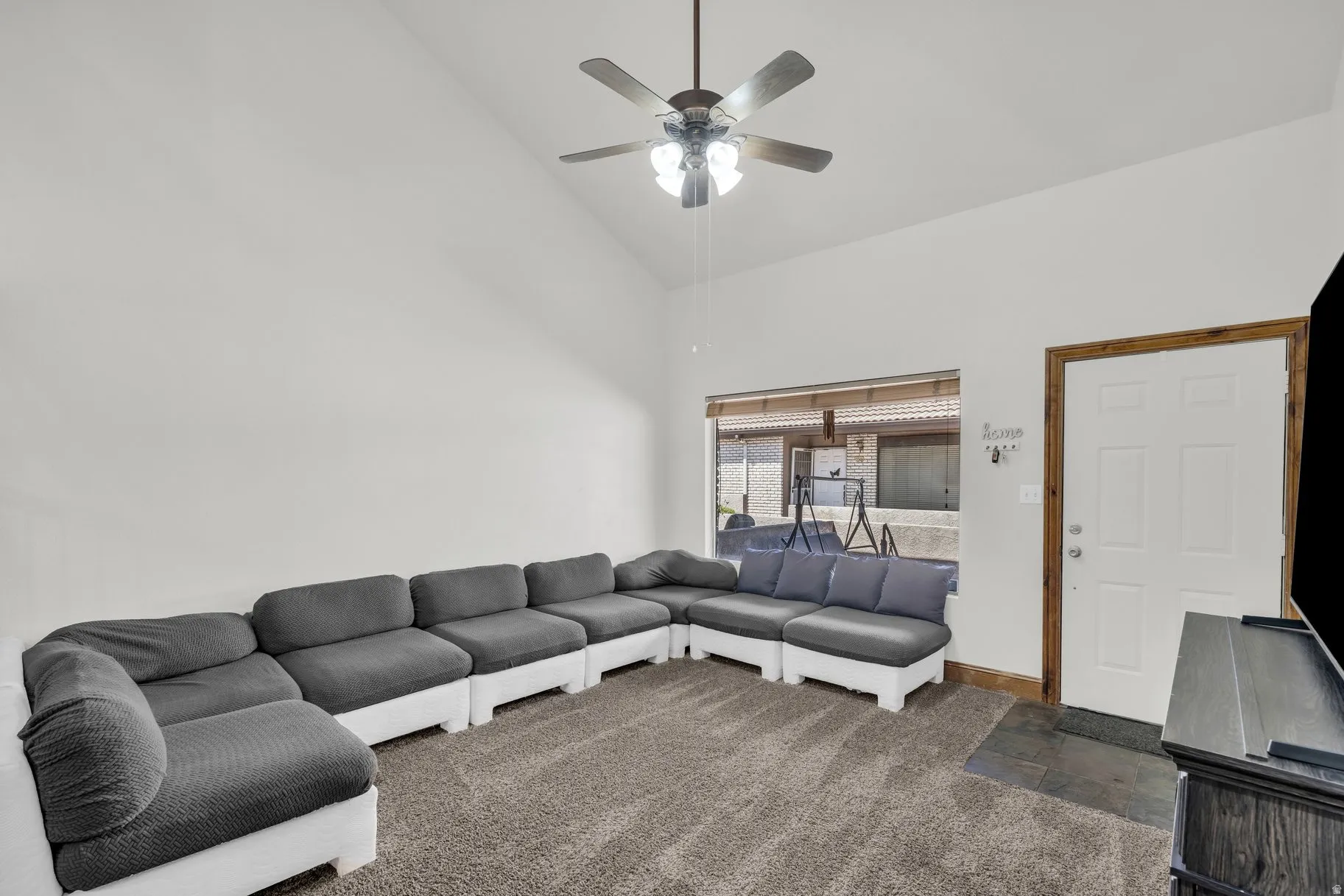 Living area with ceiling fan, vaulted ceiling, and stone finish floors