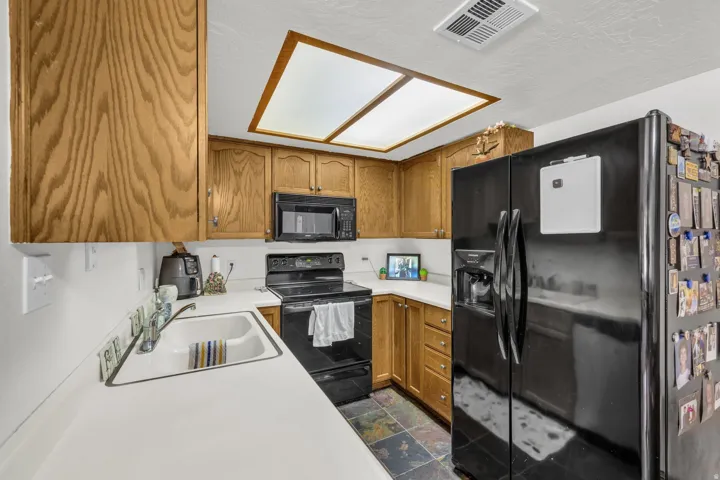 Kitchen featuring black appliances, light countertops, wood finish cabinetry, and dark stone finish flooring