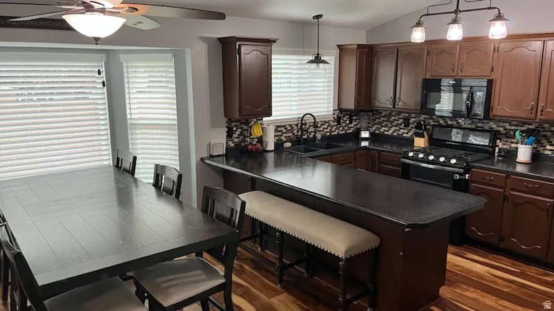 Kitchen with a breakfast bar, decorative light fixtures, black appliances, dark countertops, and lofted ceiling