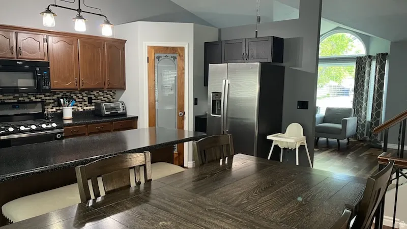 Kitchen with stainless steel fridge, black microwave, gas range, vaulted ceiling, and decorative light fixtures