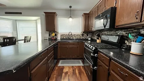 Kitchen featuring black appliances, pendant lighting, dark wood-style flooring, a peninsula, and tasteful backsplash