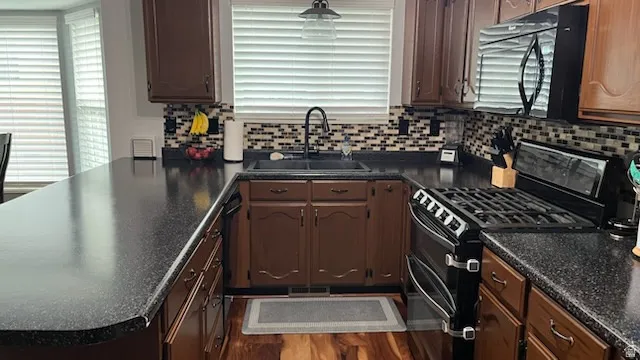 Kitchen featuring black appliances, dark countertops, a peninsula, dark wood-type flooring, and tasteful backsplash