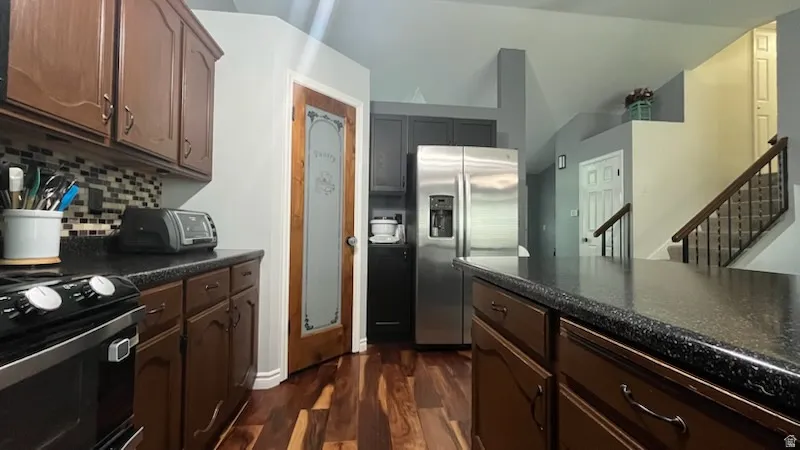 Kitchen featuring stainless steel fridge with ice dispenser, dark wood finished floors, electric range oven, decorative backsplash, and dark stone counters