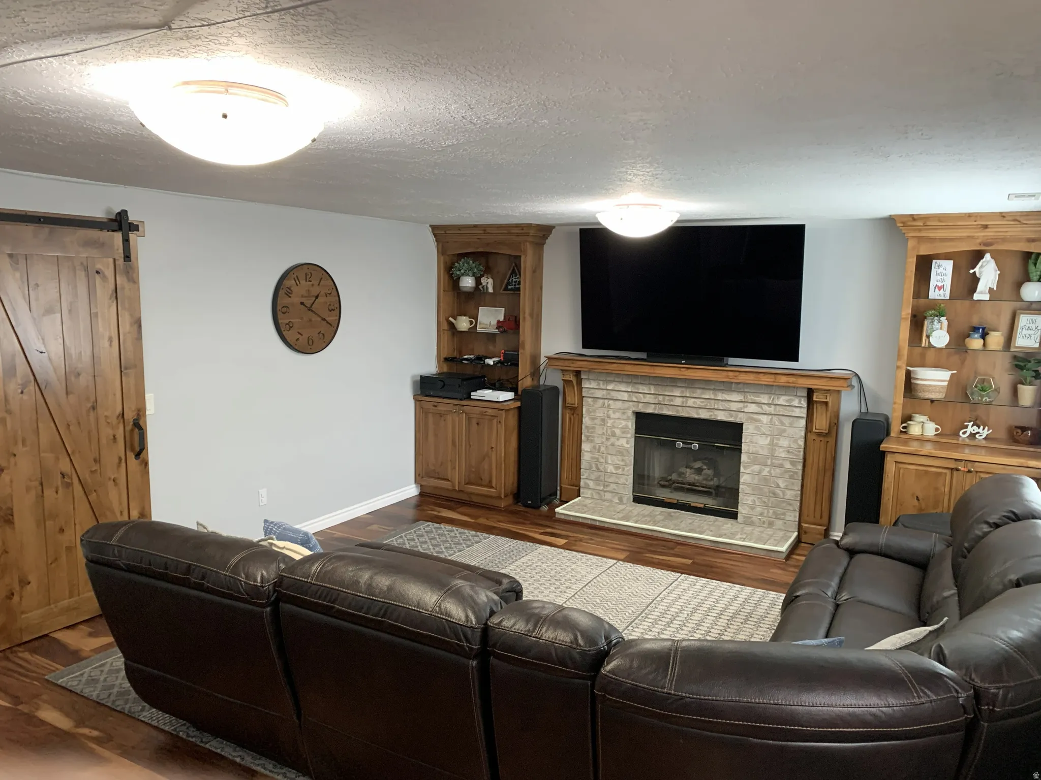 Living area with a barn door, a textured ceiling, hardwood floors, and a glass covered fireplace