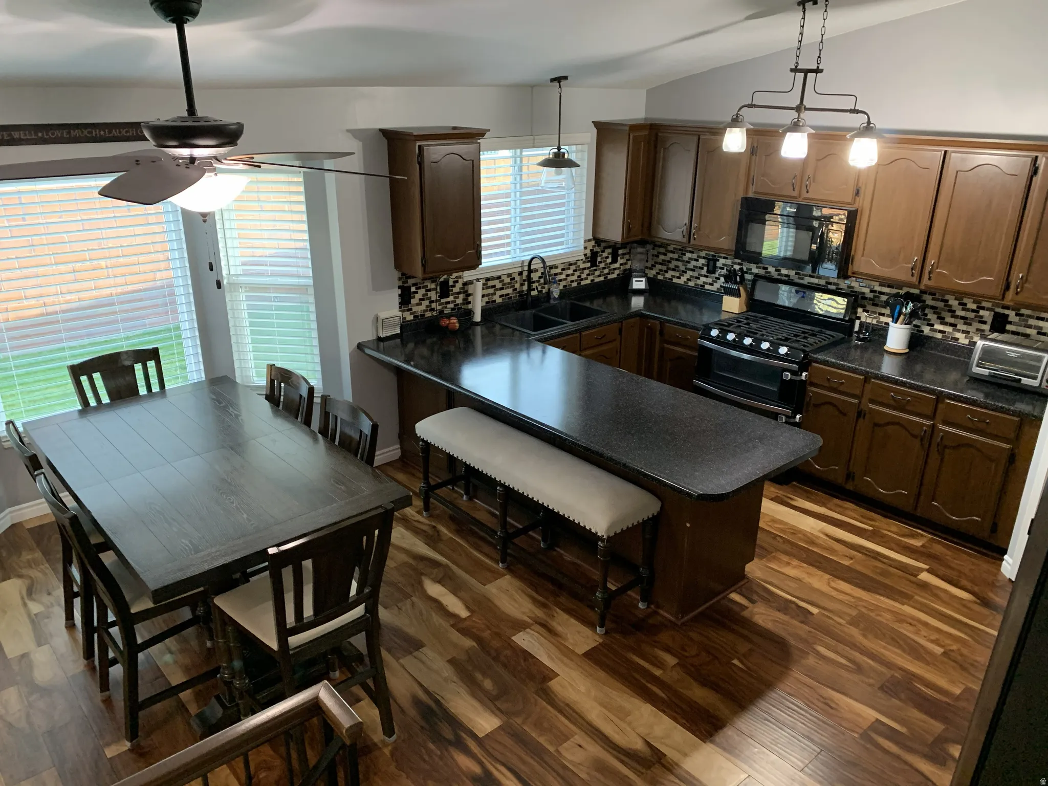 Kitchen with dark countertops, black appliances, a kitchen breakfast bar, backsplash, and vaulted ceiling