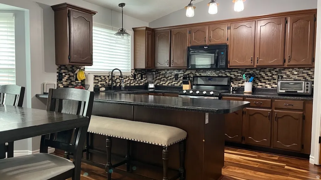 Kitchen with vaulted ceiling, dark countertops, stainless steel range oven, black microwave, and pendant lighting