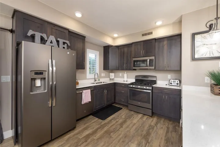 Kitchen featuring stainless steel appliances, dark wood finish cabinetry, dark wood-style flooring, pendant lighting, and light stone counters