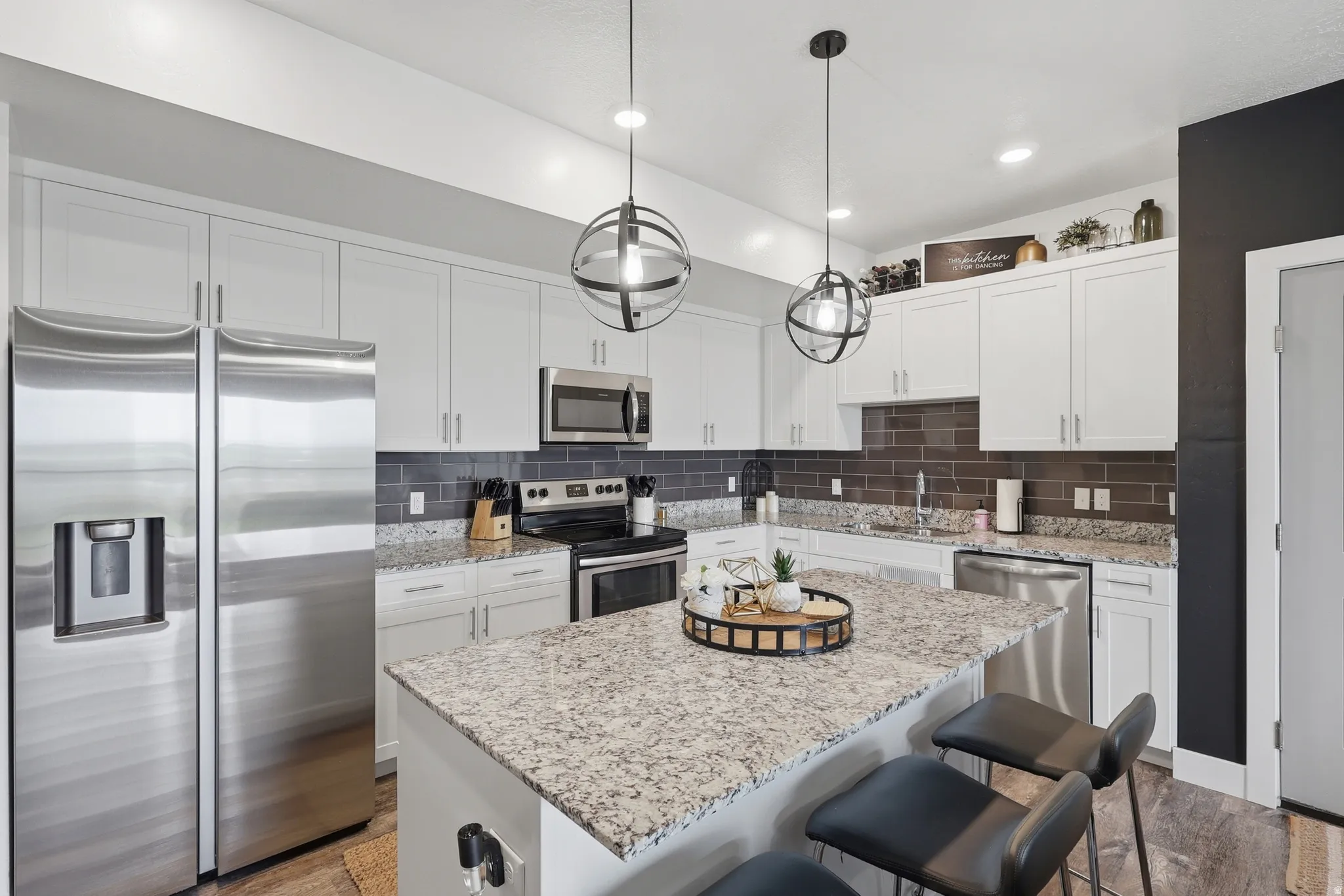 Kitchen featuring stainless steel appliances, a breakfast bar area, light stone counters, dark wood-type flooring, and a kitchen island