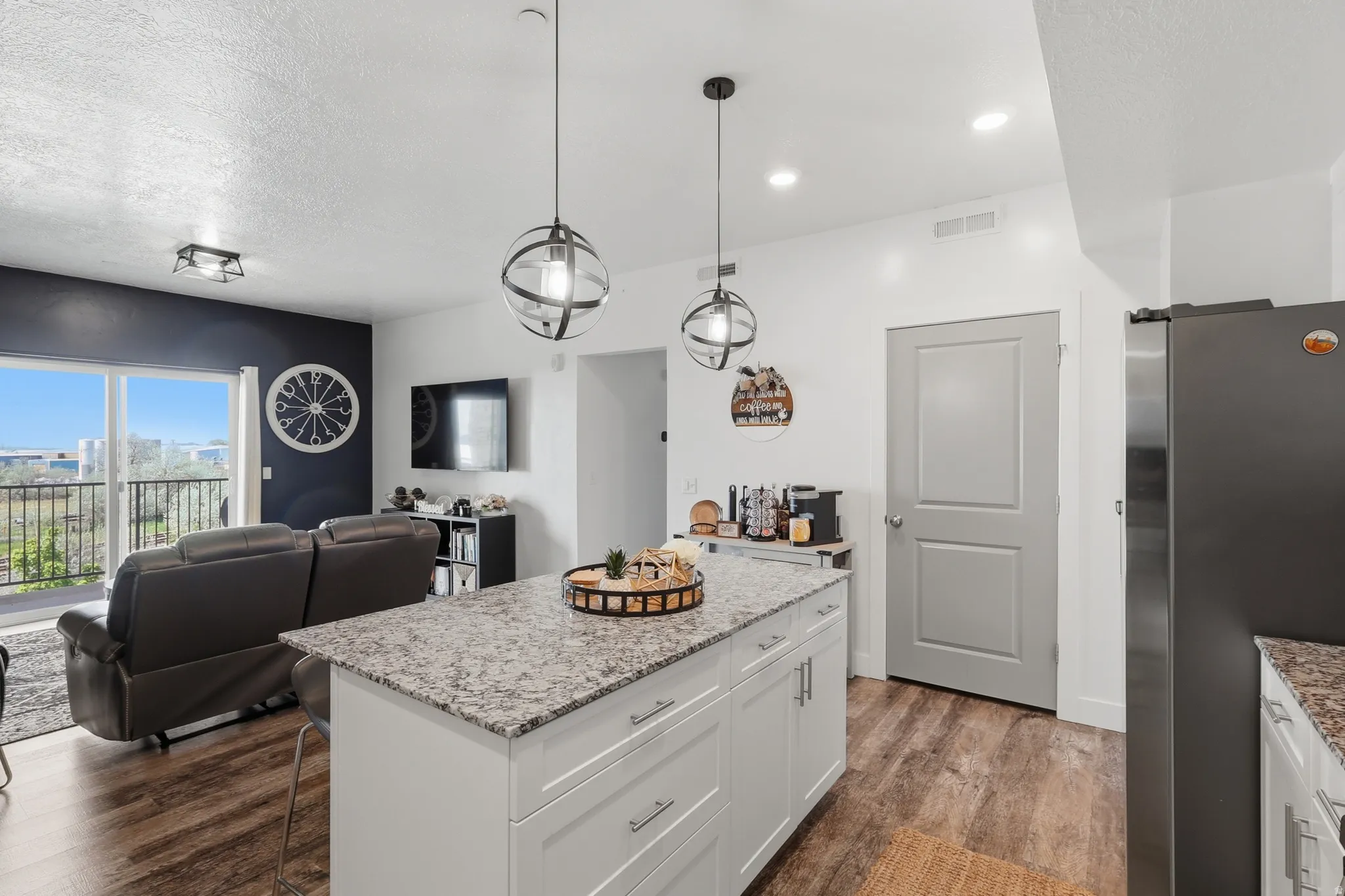 Kitchen with freestanding refrigerator, light stone counters, white cabinets, open floor plan, and dark wood-style flooring
