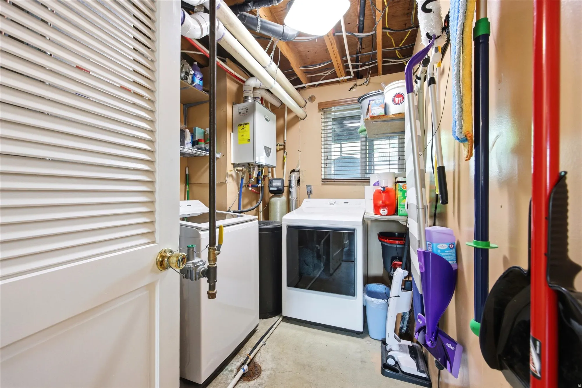 Laundry area featuring concrete flooring, washer and dryer, and tankless water heater
