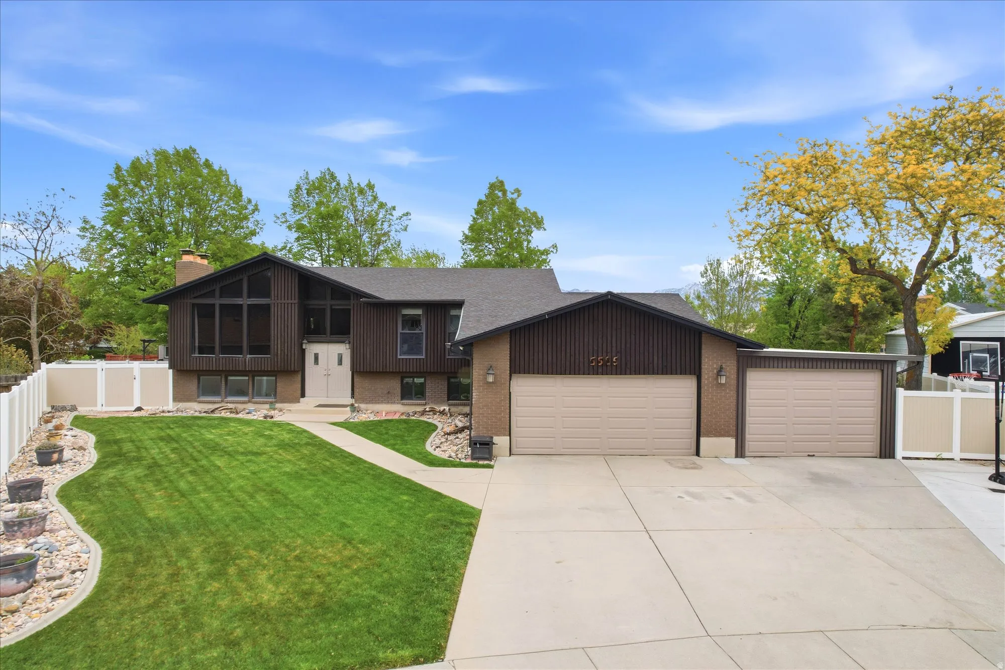 Split foyer home with an attached garage, a chimney, driveway, a sunroom, and brick siding