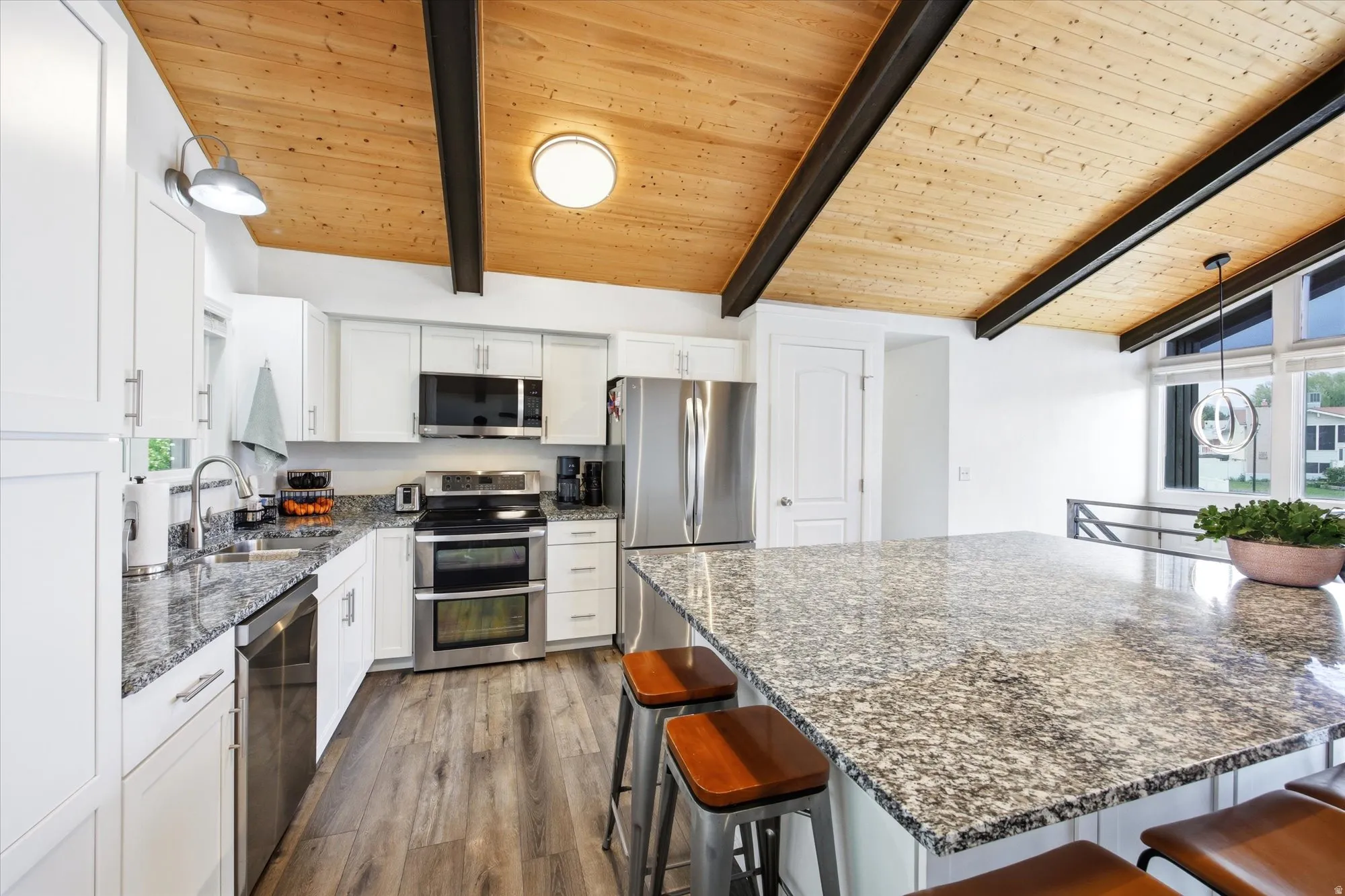 Kitchen with a kitchen bar, lofted ceiling with beams, dark stone counters, stainless steel appliances, and wooden ceiling