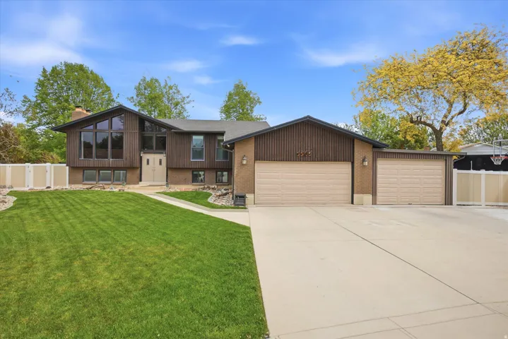 Bi-level home with an attached garage, brick siding, driveway, and a chimney