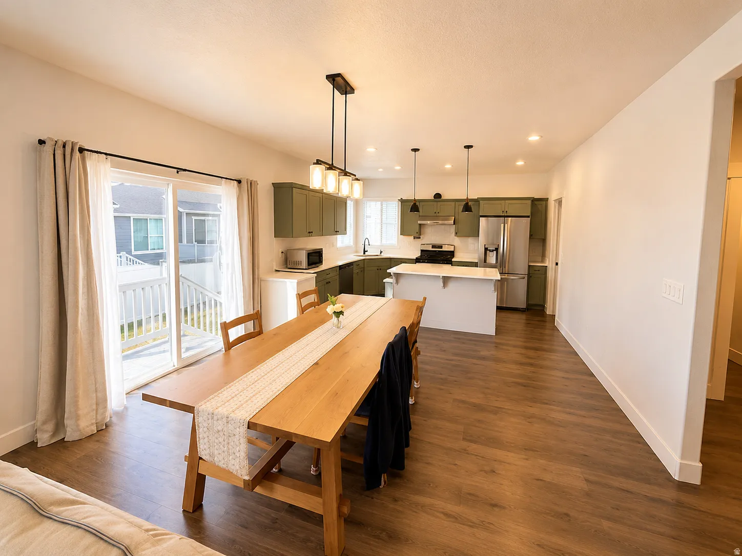 Open-concept living space featuring wood-finish flooring, a modern kitchen with sage green cabinetry, stainless steel appliances, and a central island