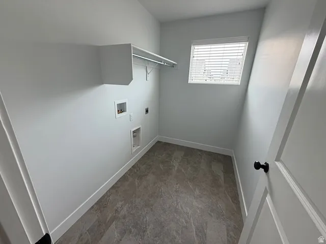 Dedicated laundry room featuring textured tile flooring, a built-in shelf with hanging rod, a window with blinds, and white baseboards